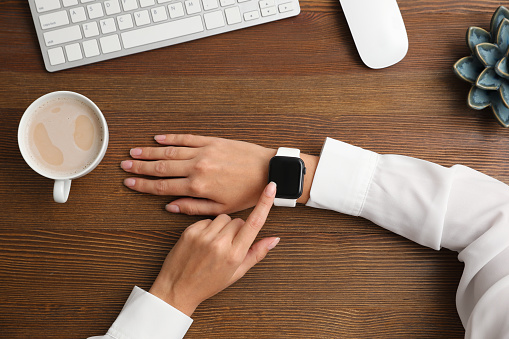 Woman using stylish smart watch at wooden table, top view