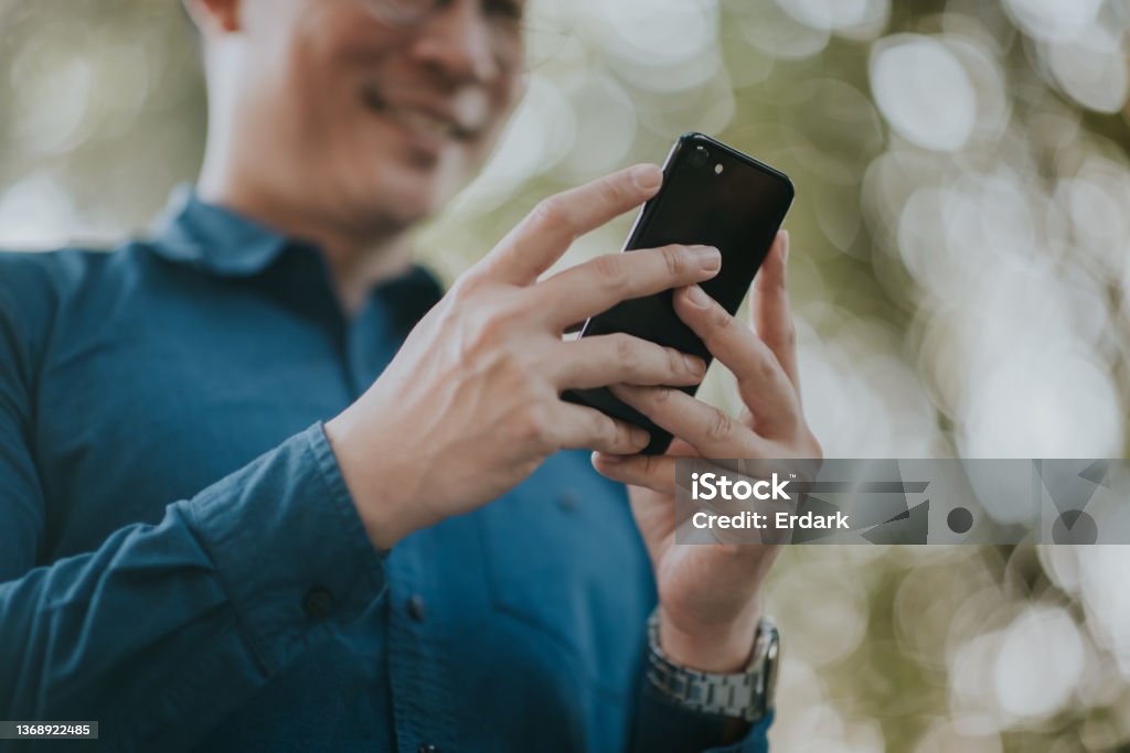 Sales manager checking order in his mobile phone. Asian sales manager on his lunch break, checking order on his mobile phone while having lunch at garden theme restaurant. Business Stock Photo