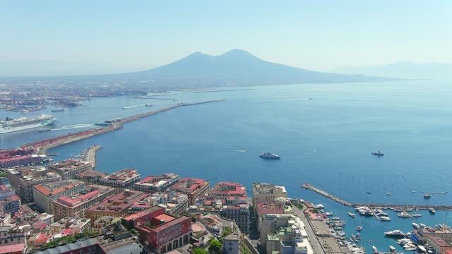 Aerial view of cityscape of Naples, historic city in Italian region of Campania, majestic cone of volcano Mount Vesuvius in background, clear blue sky - landscape panorama of Italy from above, Europe