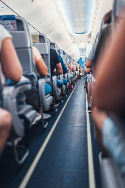 A narrow aisle between the rows of passenger seats in the cabin of a budget airliner A narrow aisle between the rows of passenger seats in the cabin of a budget airliner - a full plane of tourists is ready to fly narrow photos stock pictures, royalty-free photos & images