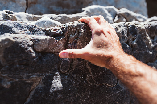 Men tenacious strong fingers cling to the unevenness of the stone - rock climbing