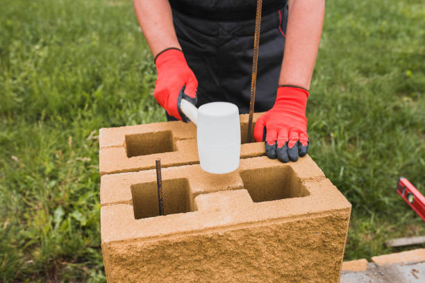 maurermeister klopft mit einem gummihammer auf einen steinblock - bau eines zaunpfostens - mason brick bricklayer installing stock-fotos und bilder