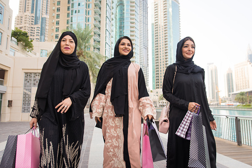 Arabic women with abaya bonding and having fun outdoors - Happy middle eastern friends meeting and talking while shopping