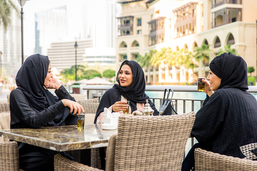 Arabic women with abaya bonding and having fun outdoors - Happy middle eastern friends meeting in a cafe and talking