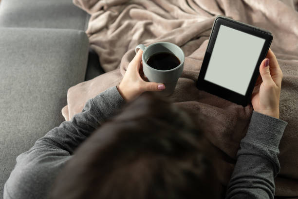 istock Unrecognizable young woman reading with an electronic book while holding a cup of coffee. 1368926546