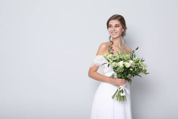 istock Young bride wearing wedding dress with beautiful bouquet on light grey background. Space for text 1368926575