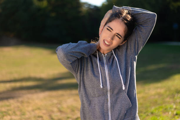 Young woman holding her painful neck after exercising in park stock photo