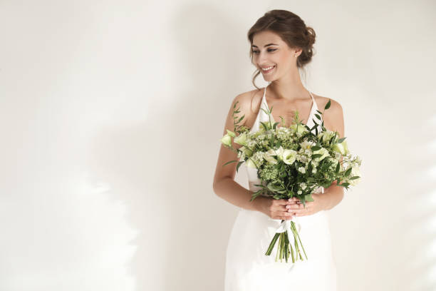 istock Young bride wearing wedding dress with beautiful bouquet on light background. Space for text 1368928655