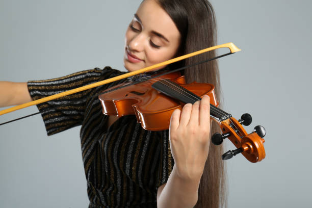 istock Beautiful woman playing violin on grey background, focus on hand 1368933862