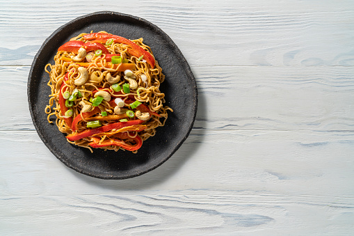 Stir fry Soba noodles vegan recipe asian food with plant based ingredients as soba noodles, onion, carrots, bell pepper, peanut butter, cashews, lime, garlic, soy sauce, sesame oil, sriracha, maple syrup, olive oil and cilantro