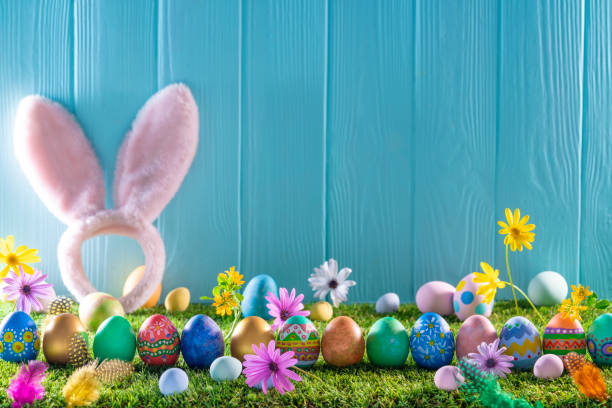 istock Easter eggs on turf grass and blue wooden wall with spring flowers 1368935270