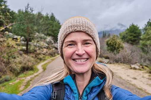 Happy woman taking a selfie portrait with smartphone on nature at winter. Portrait of a smiling girl looking at the camera