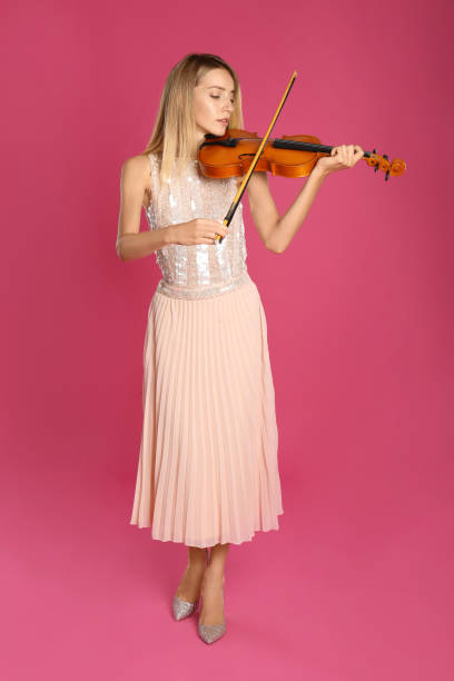 istock Beautiful woman playing violin on pink background 1368936042