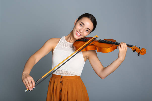 istock Beautiful woman playing violin on grey background 1368936045