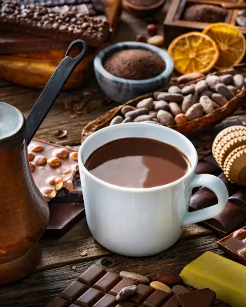 Melted hot chocolate cup with vintage copper chocolate pot and cocoa beans with assorted bars on rustic wood