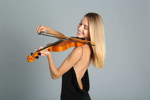 istock Beautiful woman playing violin on grey background 1368936682