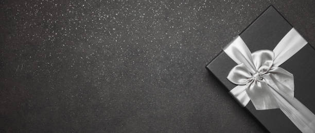 istock Black gift box with a silver ribbon and a large bow on a granite dark background. Place for the inscription 1368937524