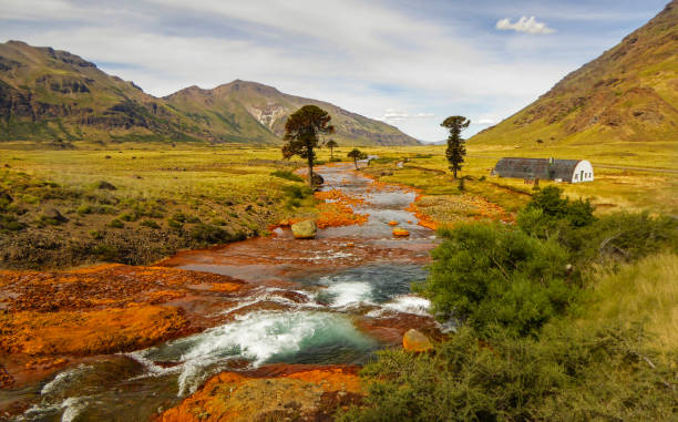 puente sobre un río con orillas anaranjadas con montañas al fondo y pehuen. río agrio, caviahue, neuquén, argentina. - neuquén fotografías e imágenes de stock