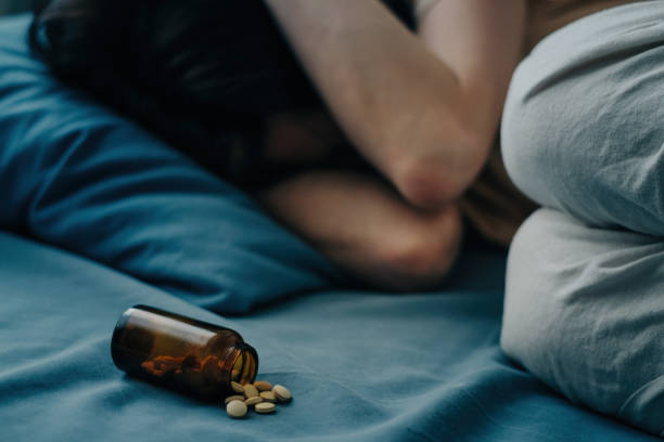 Medicines are scattered on the bed in front of woman. stock photo