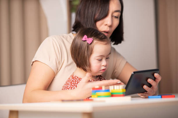 istock mom and child with down syndrome on online classes with mobile tablet 1368951977