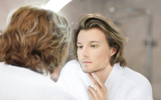 istock young man looking in the mirror,combing his hair,looking at problems on face. 1368957083