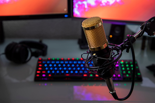 Professional microphone with gamer workstation in the background and headphones.