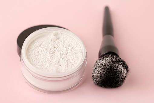 A jar of white face powder with a black brush on a gentle background.