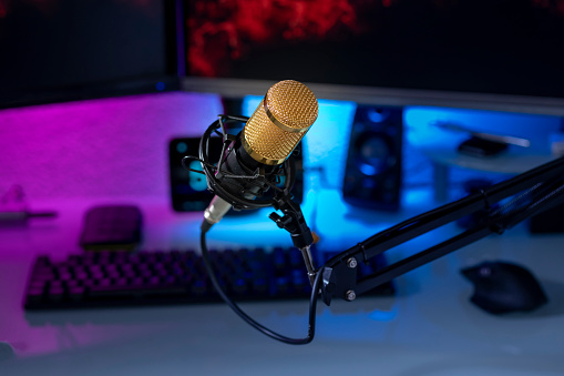Condenser microphone in gamer setup with monitors, keyboard, mouse and colored lights.