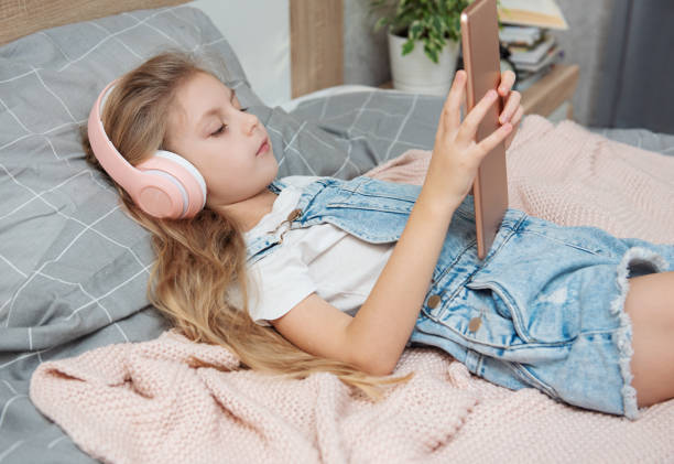 istock Cute Little girl lying on bed and using tablet at home 1368962325