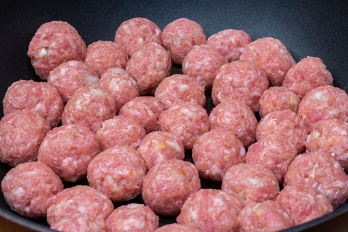 Side view on raw semi-finished minced meatballs with onion on the frying pan.