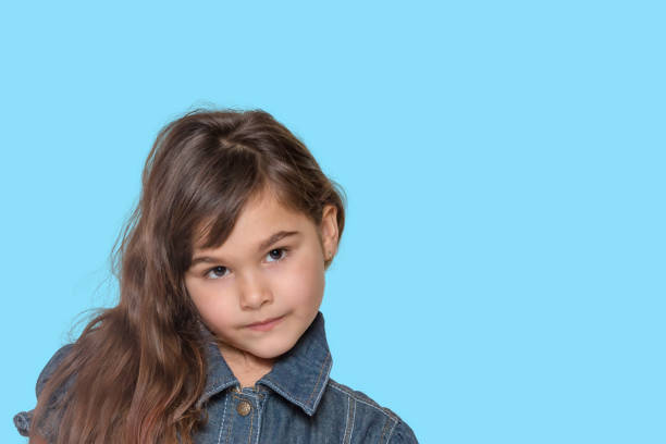 Tanned long haired little girl wears  denim costume is posing on blue background.