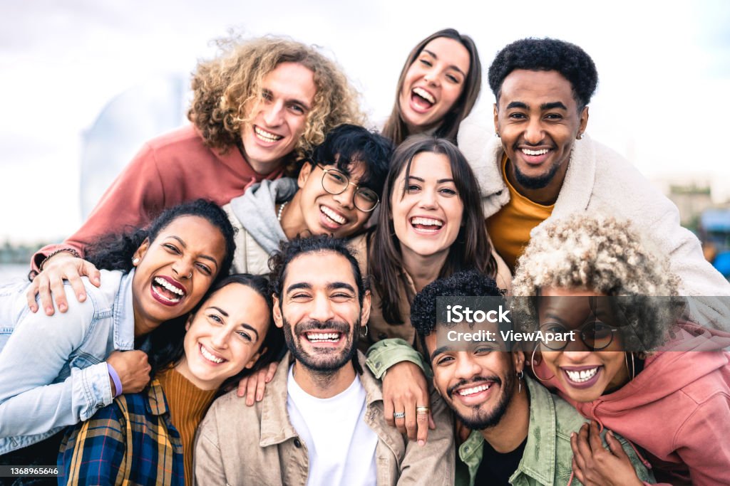 Multi ethnic guys and girls taking selfie outdoors with backlight - Happy life style friendship concept on young multicultural people having fun day together in Barcelona - Bright vivid filter People Stock Photo