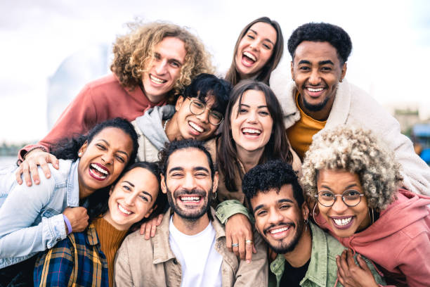 Multi ethnic guys and girls taking selfie outdoors with backlight - Happy life style friendship concept on young multicultural people having fun day together in Barcelona - Bright vivid filter stock photo