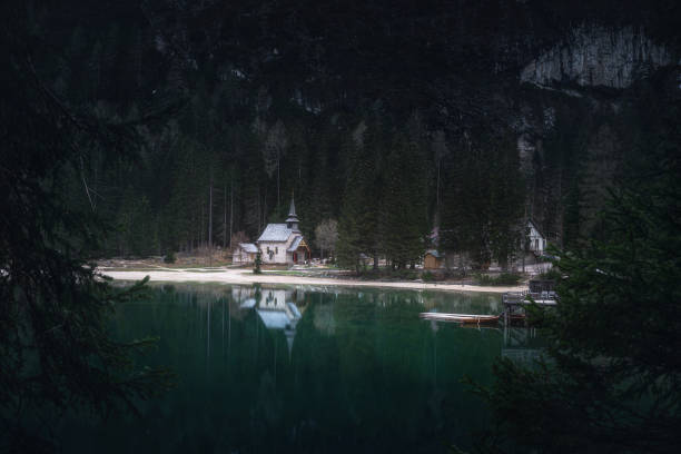 moody landscape with braies lake and church in dolomites mountains, south tyrol, alto adige, italy - woods reflection famous place standing water imagens e fotografias de stock