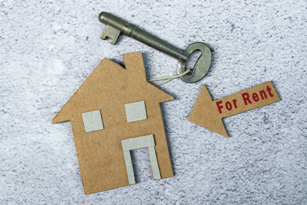 For rent text on brown arrow and paper house model with key on floor tiles stock photo