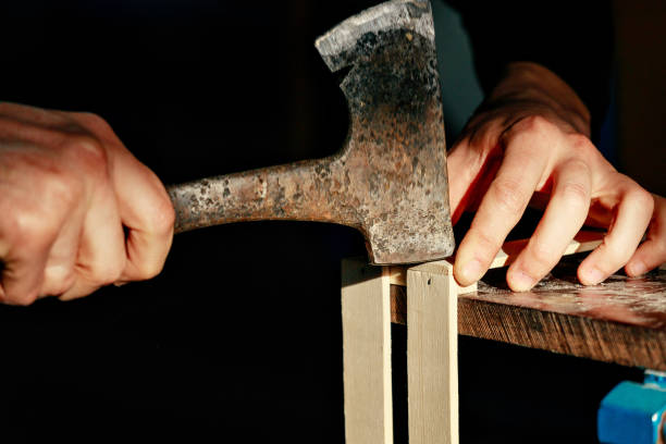 istock Carpenter at workbench nails down small wooden box.Hands of worker with old axe.Authentic workflow in carpentry workshop 1368970186
