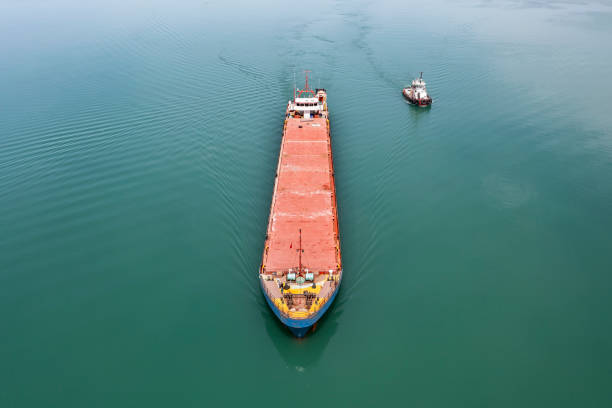 luftaufnahme des frachtschiffs, das sich dem hafen mit dem schlepper nähert. luftaufnahme des frachtschiffes auf der durchreise. - piloting commercial dock harbor industrial ship stock-fotos und bilder