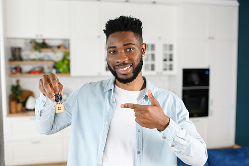 Key in hand of happy young multiracial man. Cheerful male moved in new house, rent apartment, bought own real estate, the key with keyring in shape of little house