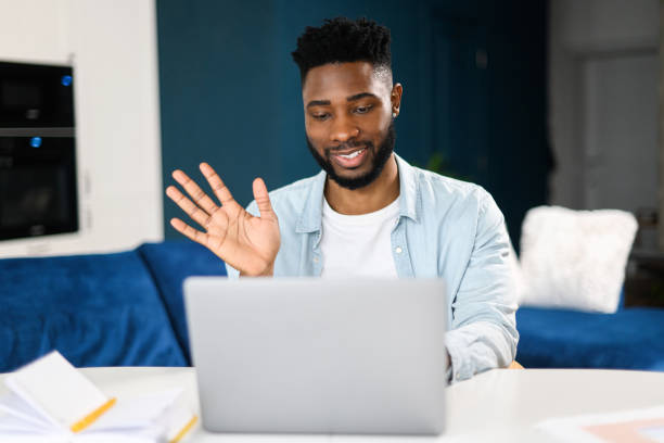 istock Video call. Cheerful attractive multiracial guy is using laptop for video communication, while sitting at the table in modern flat and waving into webcam 1368977724