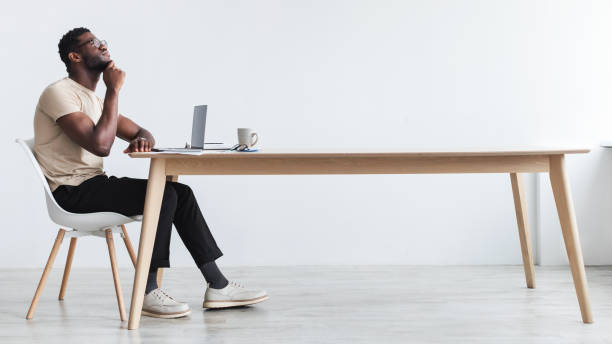 istock Pensive young black guy using laptop, sitting at desk, thinking over something, working online from home office 1368979706
