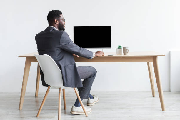 istock Black businessman in formal suit sitting at table, working with computer, mockup for website design 1368981100