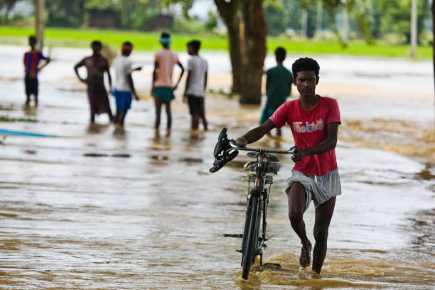 westbengalische flut 2021 - überflutete landschaft und ureinwohner überqueren überflutete autobahnen - shoe men indian culture indian ethnicity stock-fotos und bilder