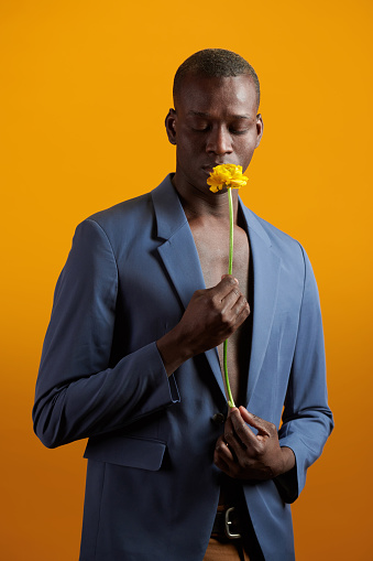 Portrait of African handsome man in suit smelling the flower in his hand standing against the yellow background