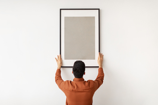 istock Young man hanging picture frame on the wall 1368982167