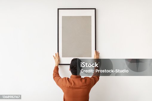 istock Young man hanging picture frame on the wall 1368982167