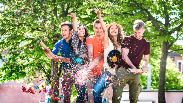 amis heureux et amusés s’amusant à côté en acclamant avec des confettis - les jeunes profitent du printemps et de l’été ensemble à la garden-party - concept de style de vie des jeunes sur un filtre chaud et vif et lumineux - music festival park friendship summer photos et images de collection