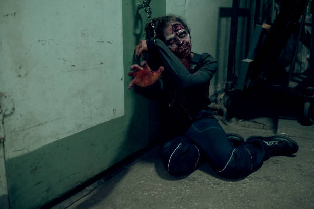 Full length shot of female zombie chained to wall in dark room and reaching to camera, copy space