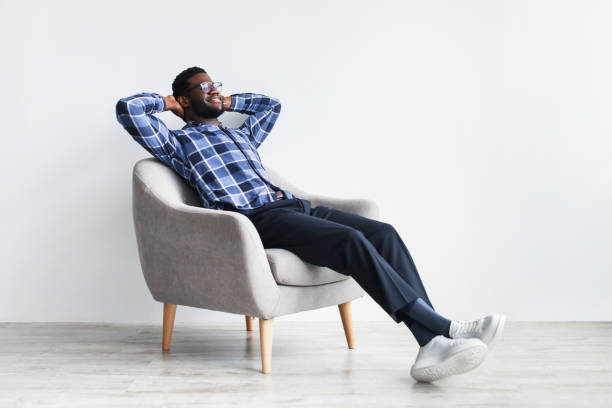 istock Peaceful young black man relaxing in armchair against white studio wall, free space 1368985431