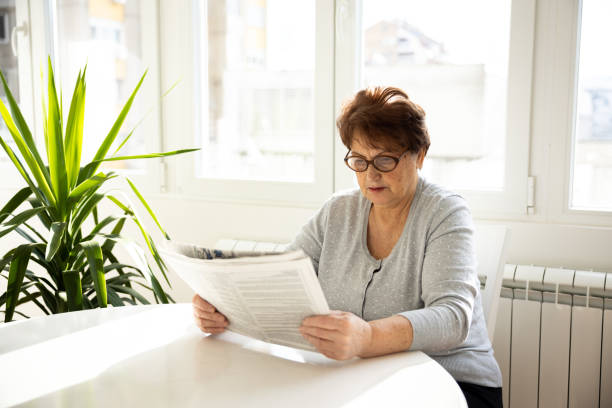 istock Senior woman reading newspaper at home 1368986309