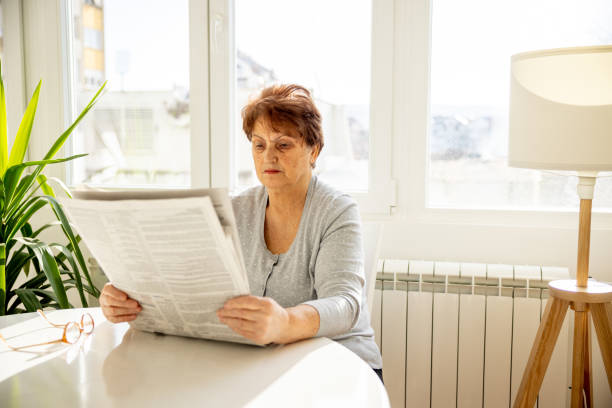 istock Senior woman reading newspaper at home 1368986446